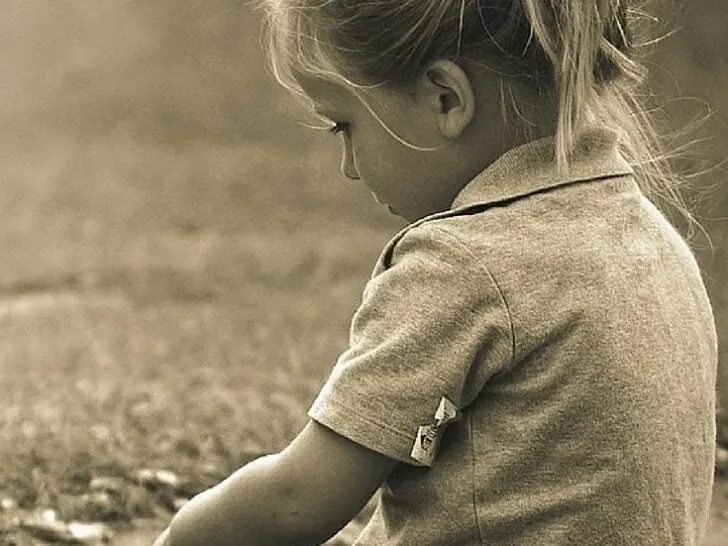 a young girl sitting and staring at the ground&nbsp;