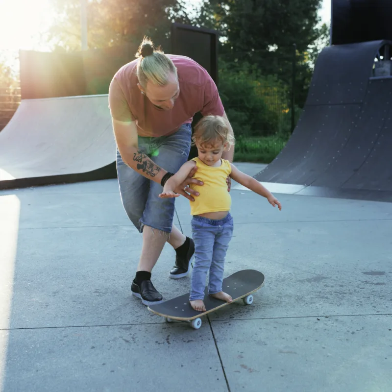 a little boy learning how to skateboard with his dad