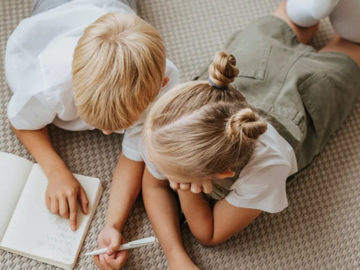 Two-children-writing-in-a-journal-lounging-on-a-floor